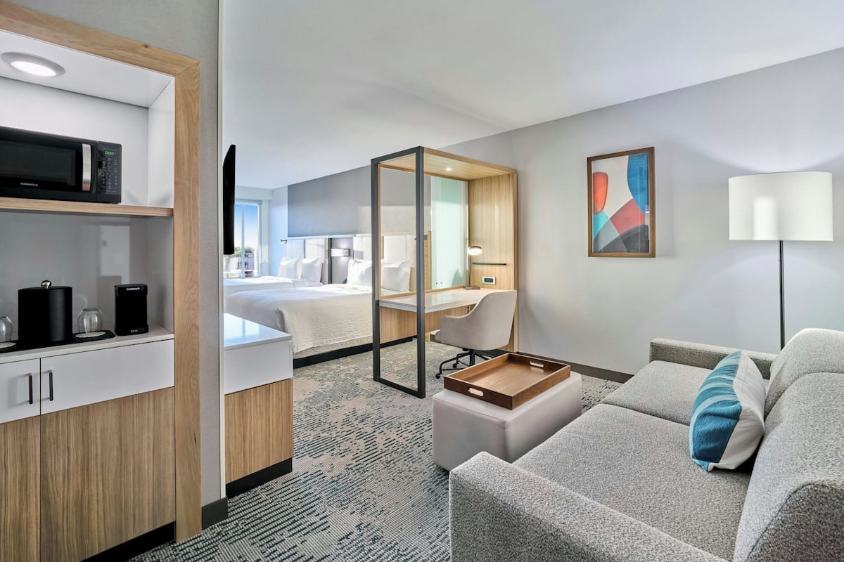 A hotel room with a bed, a desk, a sofa, a microwave, a TV, and a painting on the wall.