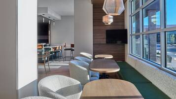 A modern interior with round tables and cushioned seating, a flat-screen TV mounted on the wall, and large windows offering a view outside.
