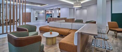 A modern hotel lobby with seating areas, a reception desk, and a bar.
