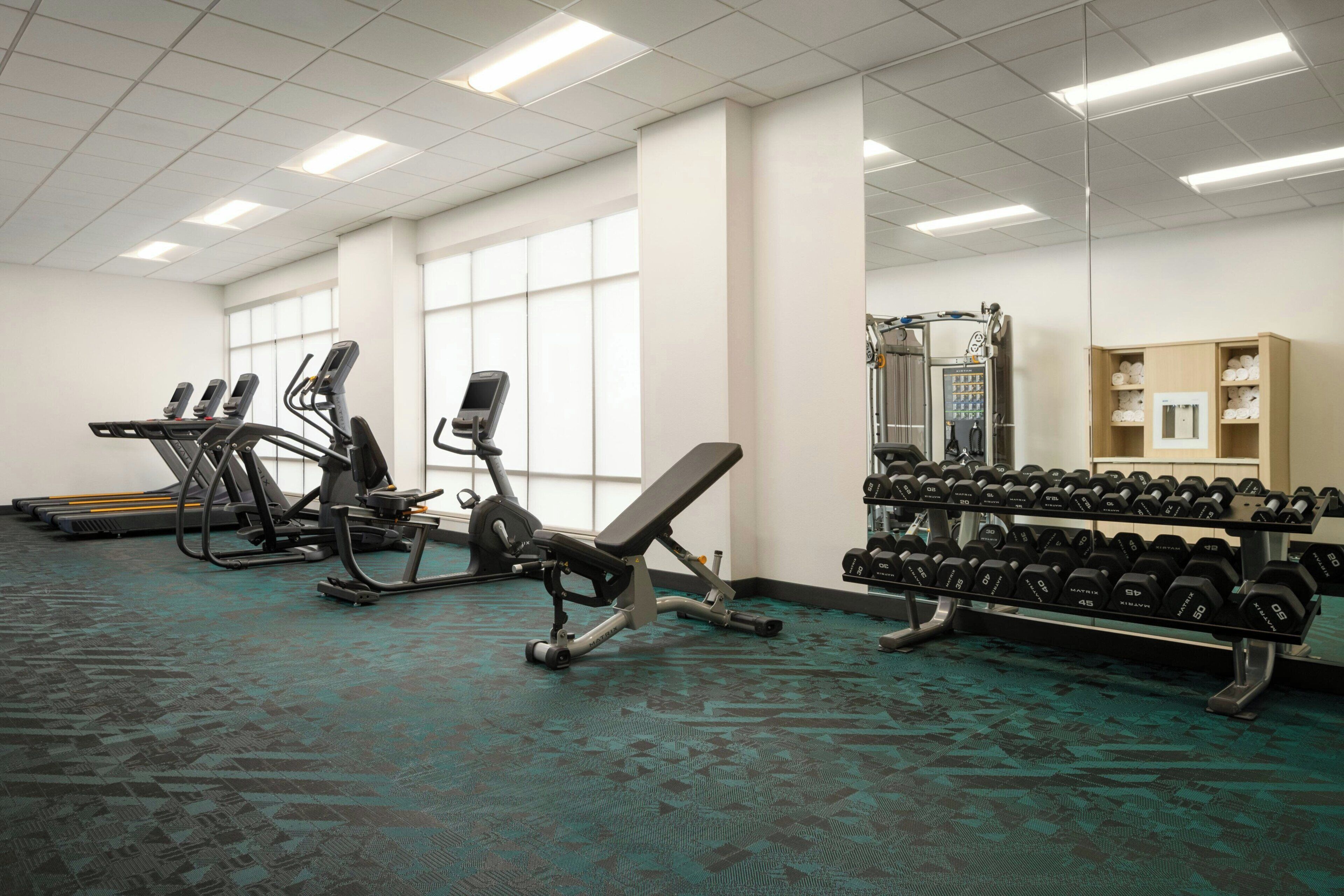 Ein Fitnessraum mit Laufbändern, Crosstrainern, einer Hantelbank und einer Dumbbell-Halterung.