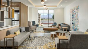 A modern living room with a sofa, armchairs, a coffee table, and a rug. There is a large window with a mountain view.