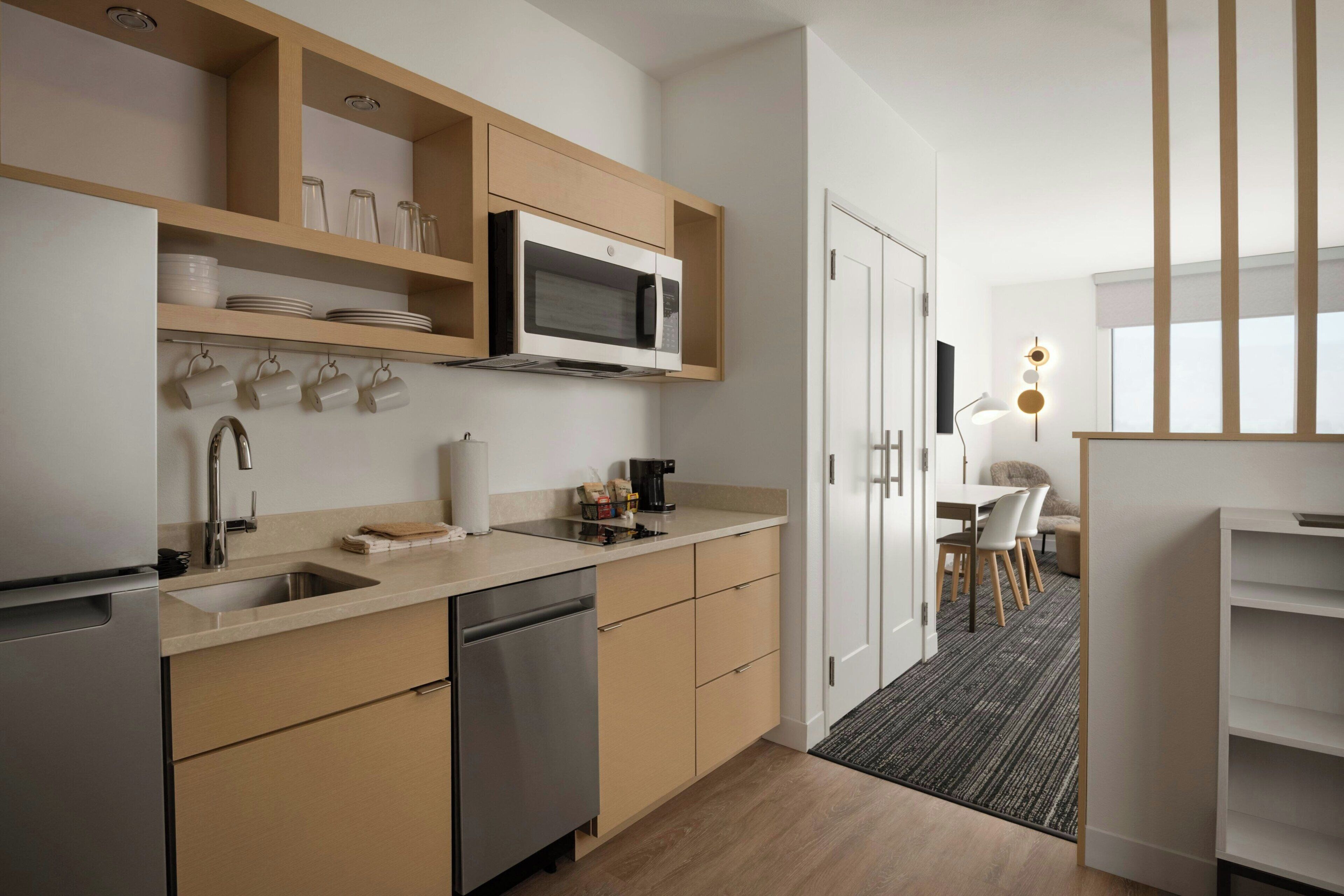 A modern kitchen with a dishwasher, microwave, and wooden cabinets. There is a dining area with a table and chairs.