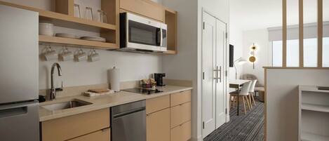 A modern kitchen with a dishwasher, microwave, and wooden cabinets. There is a dining area with a table and chairs.