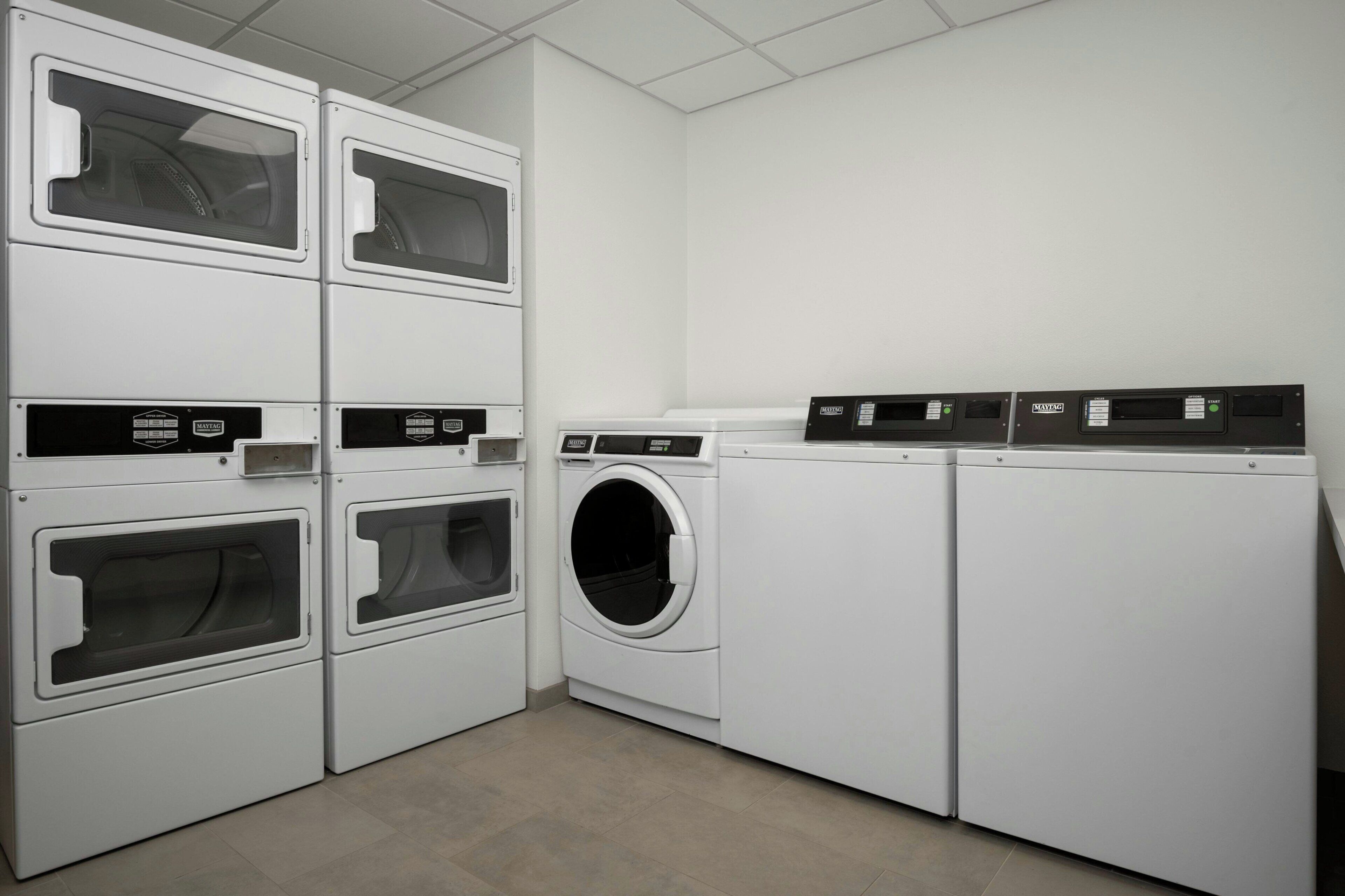 A laundry room with stacked washers and dryers, a control panel, and a tiled floor.