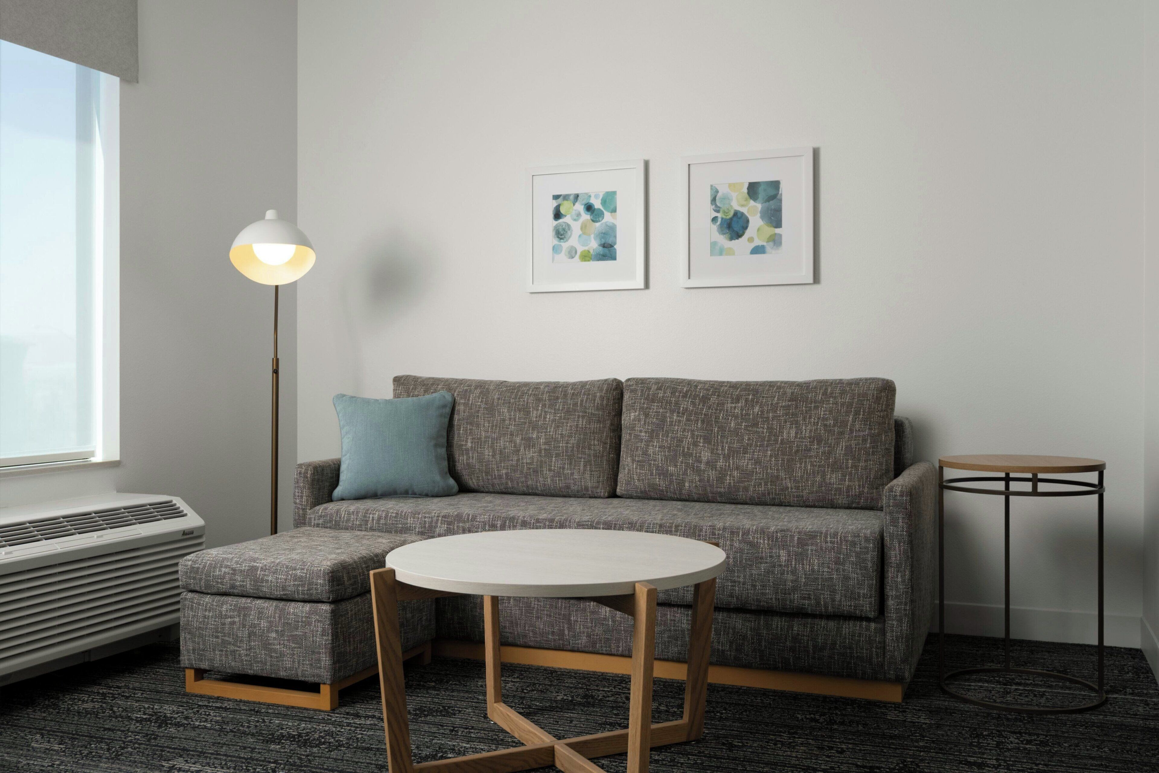 Un salon moderne avec un canapé gris, une table ronde blanche, un lampadaire et deux tableaux abstraits accrochés au mur.