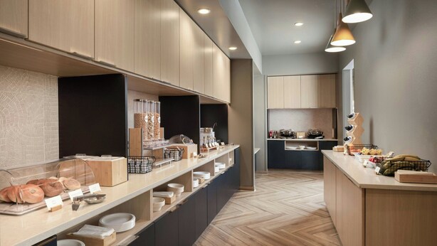 A modern kitchen with wooden cabinets, a long counter with various food items, and a herringbone floor pattern.