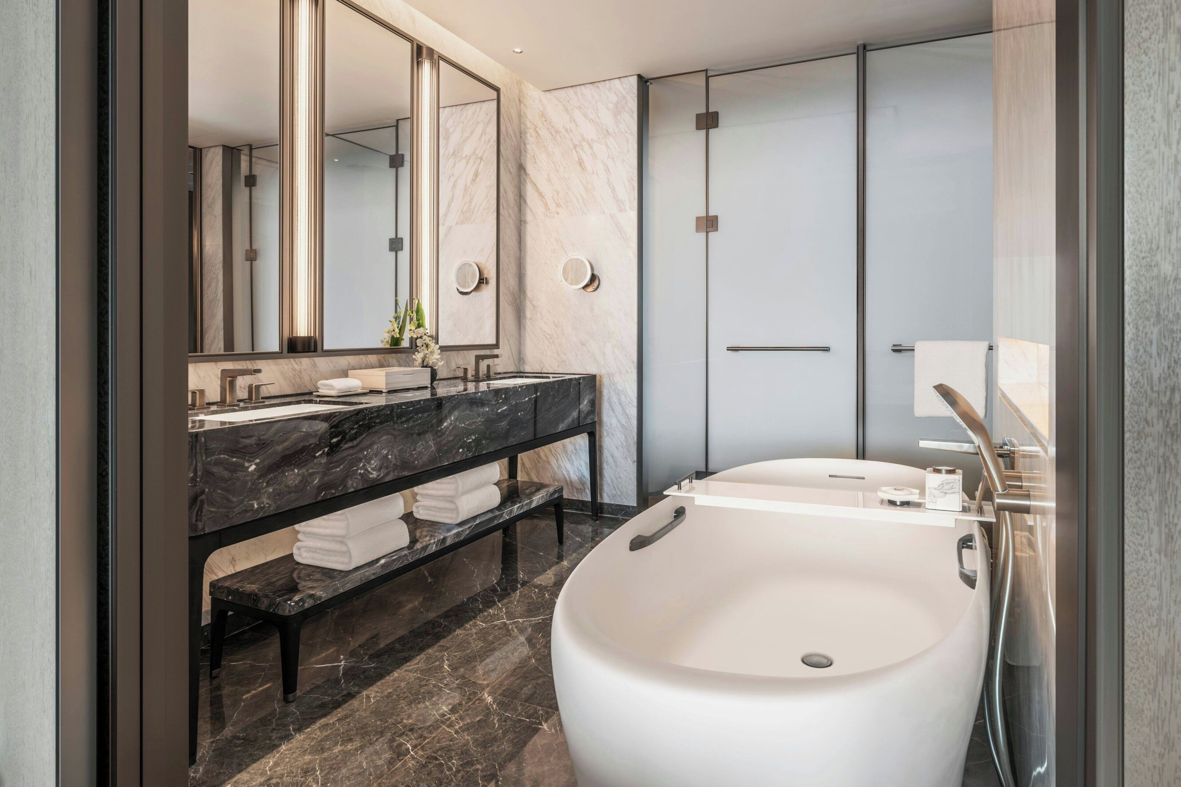 Une salle de bain moderne avec une grande baignoire, un meuble-lavabo en marbre et un grand miroir.