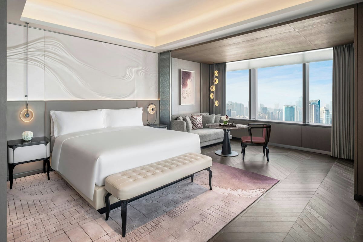 A modern hotel room with a large bed, a sofa, a small table, and a view of the city.