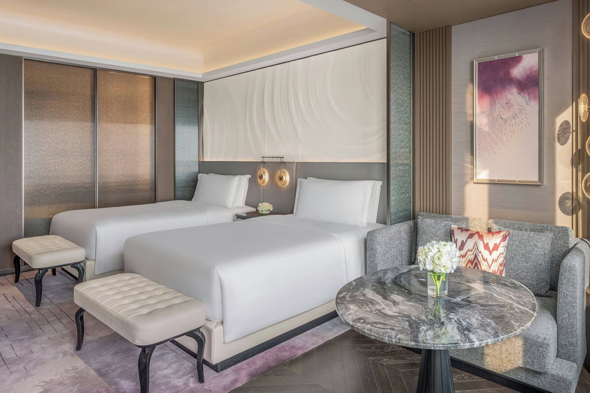 A modern hotel room with two beds, a sofa, a round marble table, and a decorative wall piece.