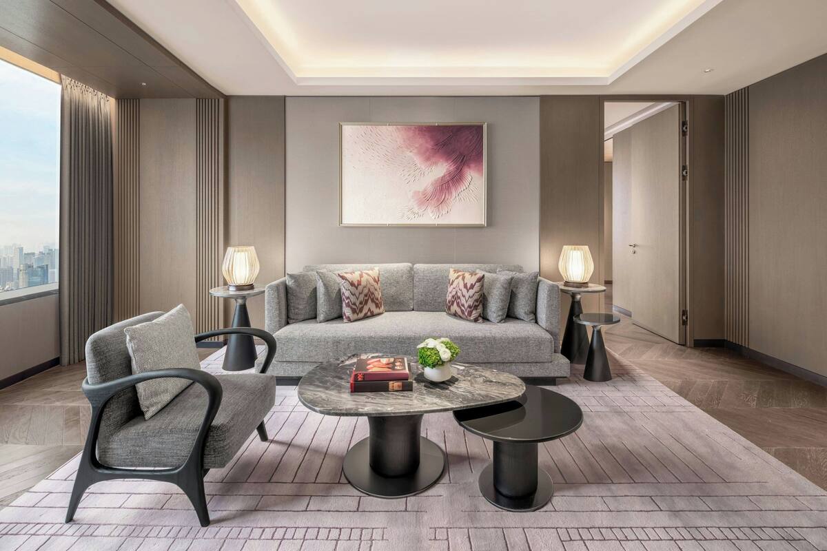 A modern living room with a grey sofa, two armchairs, a round coffee table, and two side tables with lamps.