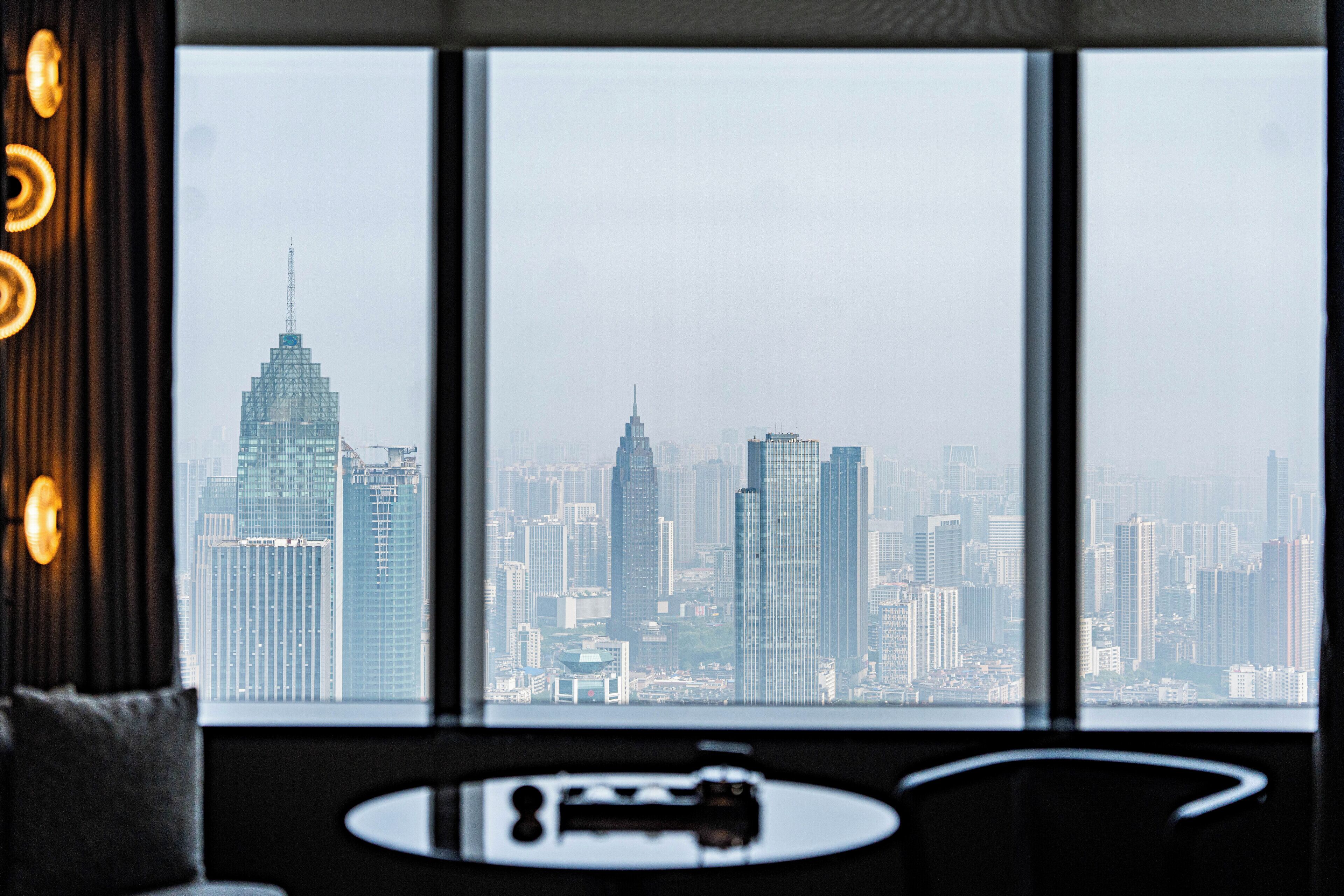 A cityscape view from a room with a large window, a sofa, and a small table with a decorative item.