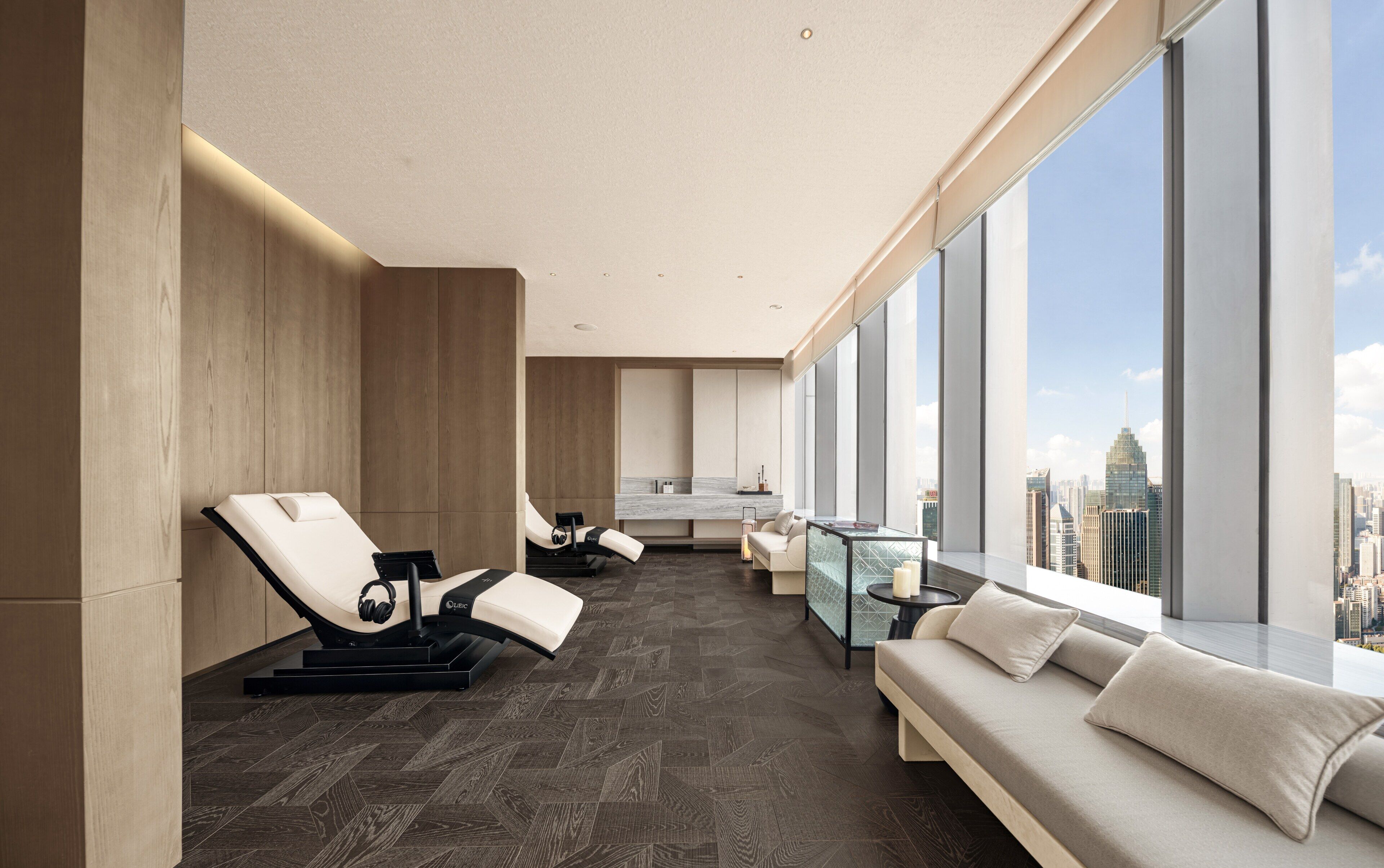 Habitación de hotel moderna con vista a la ciudad, un sillón de masaje, un sofá y una mesa de vidrio.