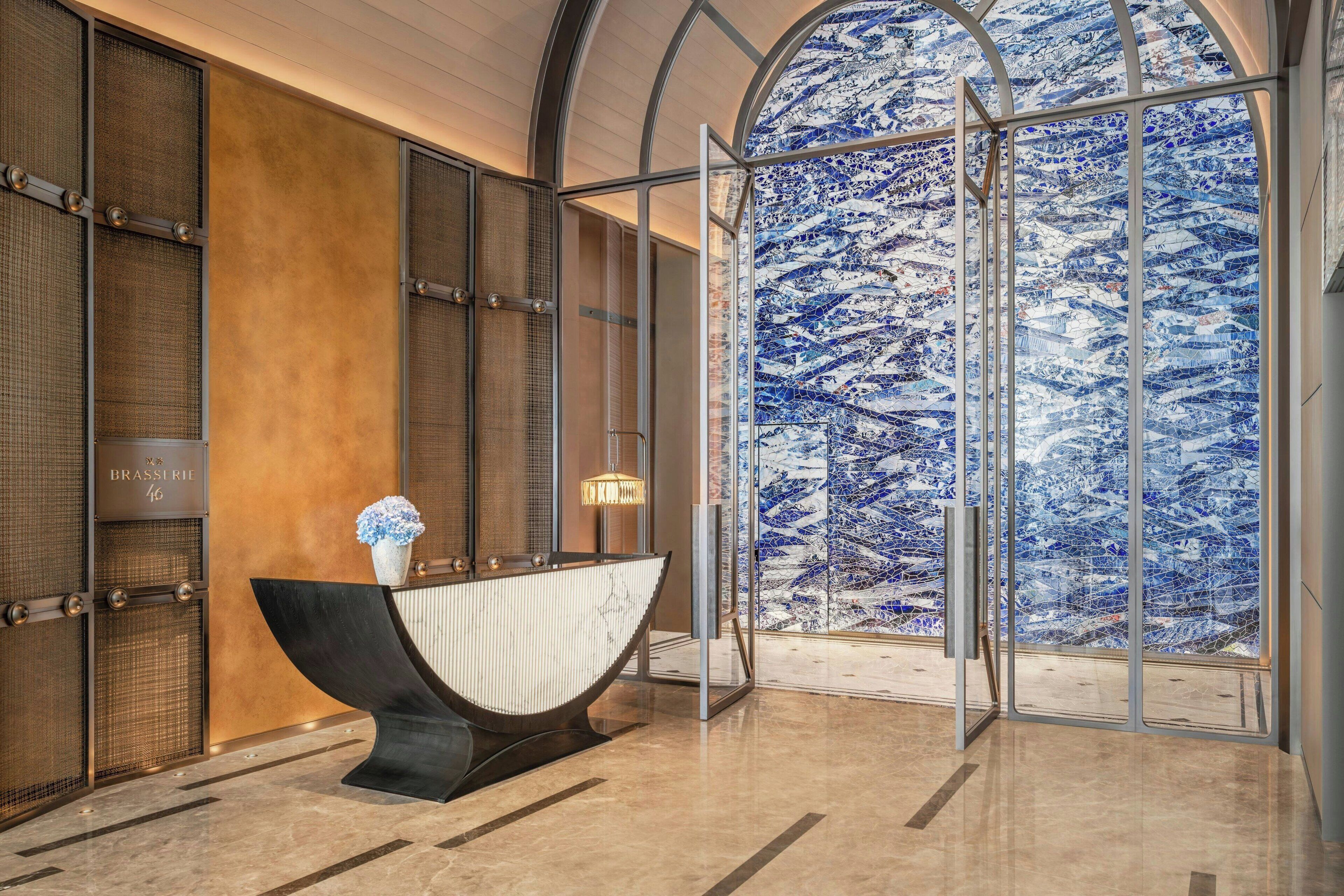 A lobby with a reception desk, a large glass door, and a view of a blue mosaic wall.
