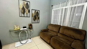 Een woonkamer met een bruine bank, een glazen salontafel met decoratieve items, en wanddecoratie.