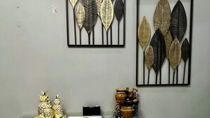 A room with a glass table displaying decorative items, a framed artwork of leaves on the wall, and a marble-patterned mat on the floor.