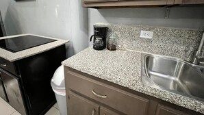 Eine kompakte Küchenzeile mit einer Arbeitsplatte aus Granit, einer Kaffeemaschine, einem Spülbecken und einem Mülleimer.