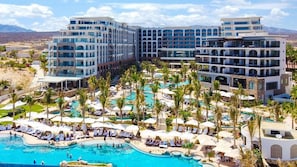 Resort com várias piscinas, palmeiras e arquitetura moderna.