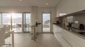 A modern kitchen with a view of the sea, a dining area with a table and chairs, and a balcony with a view of the sea. - Aziadé Horizons - Ocean View (Nazaré)