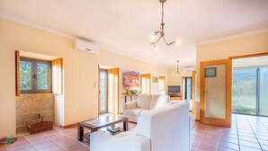A spacious living room with a sofa, a coffee table, and a TV. There are large windows and a sliding glass door leading to a balcony. - Casa Quinta de Agriboa (Ponte de Lima)