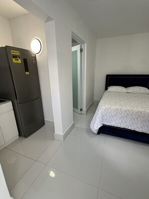 Ein kleines Hotelzimmer mit einem Bett, einer kleinen Küchenzeile inklusive Kühlschrank und einer Tür zu einem weiteren Raum.