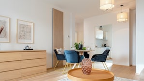 Un salon moderne avec une table basse en bois, des chaises bleues, un tapis blanc et une cuisine en arrière-plan.