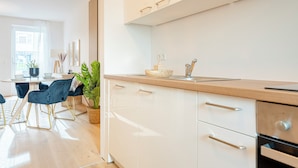 Une cuisine moderne avec des meubles blancs, un plan de travail en bois et un coin repas avec des chaises bleues et une table.