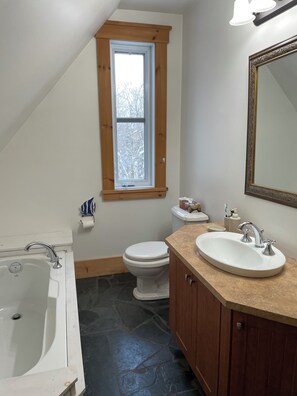 Un baño con bañera, lavabo e inodoro. Hay una ventana sobre el inodoro y un espejo sobre el lavabo.