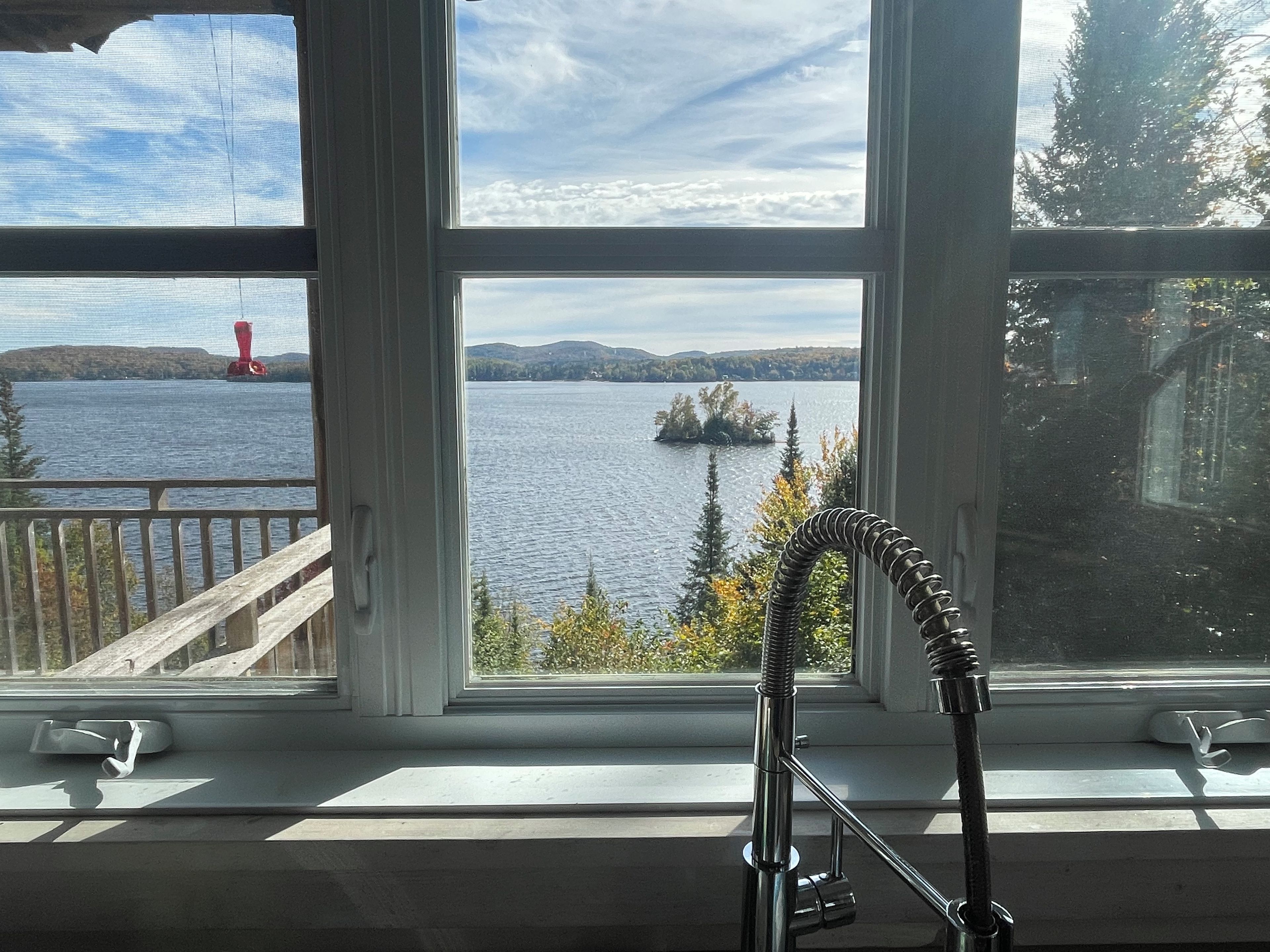 A window with a view of a lake, a red buoy, and a distant island.