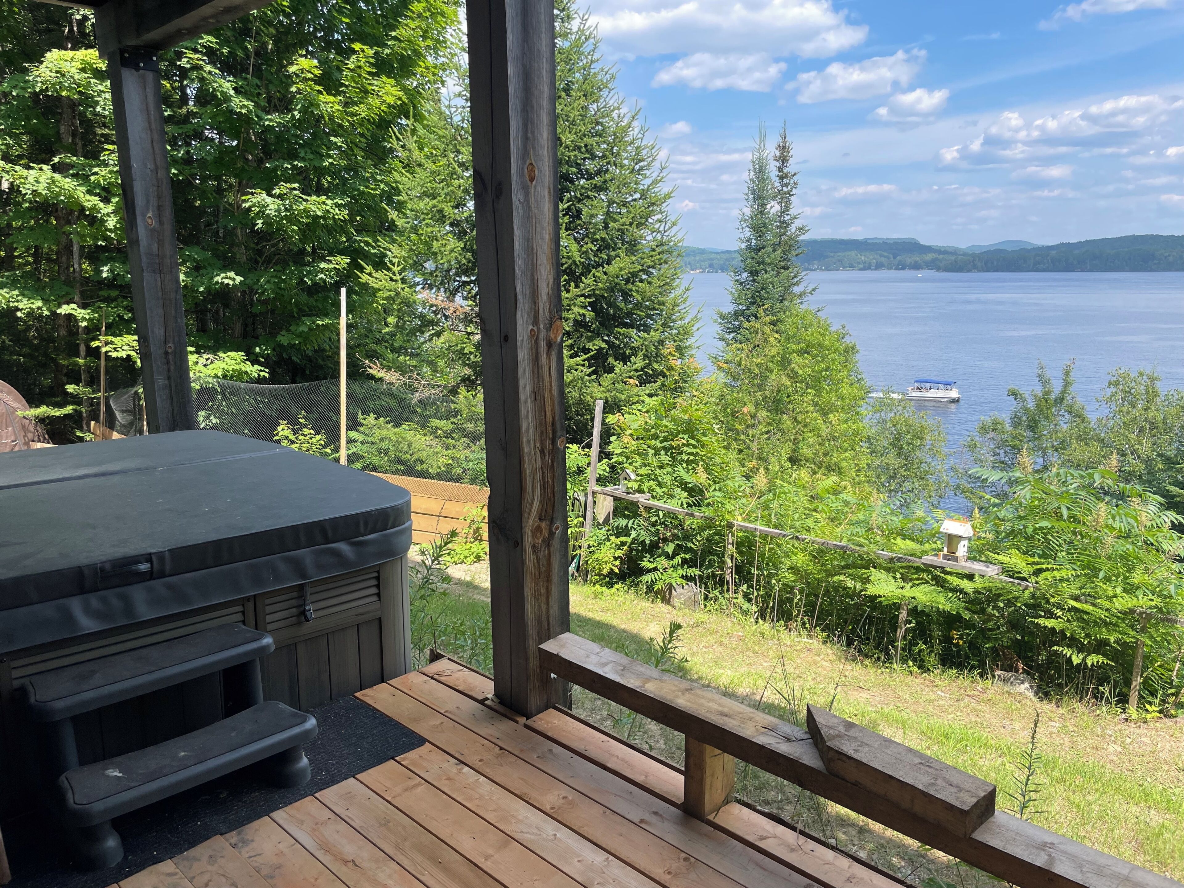 A wooden deck with a hot tub, overlooking a lake with a boat.
