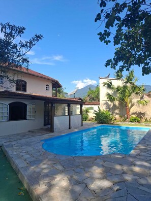 Una piscina con baldosas de piedra, un porche cubierto y vistas a montañas al fondo.