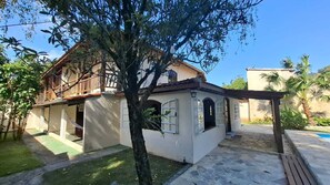 Una casa de dos pisos con un balcón, una estructura pequeña adosada con ventanas y un área de piscina.