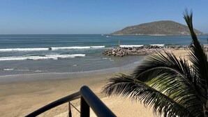 Una playa con un promontorio rocoso y una palmera al frente.