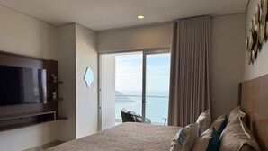 Habitación de hotel con una cama grande, un televisor de pantalla plana montado en la pared y un balcón con vistas al mar.