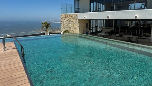 Un hotel moderno con una piscina cristalina, un muro de piedra y vistas al océano.