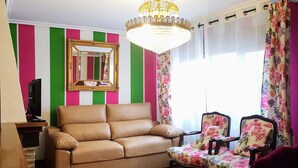 Ein Wohnzimmer mit einem beigefarbenen Sofa, einem blumigen Sessel, einem Holztisch, einer Chandelierleuchtre und einem Spiegel an der Wand.