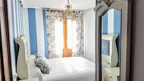 Ein Schlafzimmer mit einem Bett, floralen Vorhängen, einer Kristallleuchter und einem Spiegel.