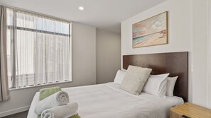 A hotel room with a large bed, a headboard, a painting on the wall, and a window with curtains. - The Alps Two Bedroom - Spacious escape right in the centre of Queenstown! (Queenstown)