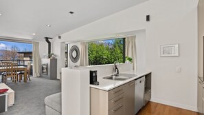 A modern kitchen with a built-in island, stainless steel appliances, and a large window offering a view of greenery. - The Alps Two Bedroom - Spacious escape right in the centre of Queenstown! (Queenstown)