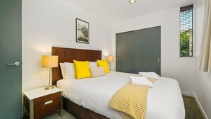 Una camera da letto ordinata con un letto, lampade da comodino, un comodino, un armadio e una finestra con tende.