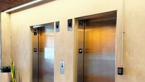 Un área de ascensores moderna con dos ascensores, un panel de control y plantas en macetas.
