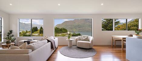 Un salon moderne doté d’un grand canapé, d’une table basse ronde et offrant une vue sur les montagnes et un lac grâce à de grandes fenêtres.