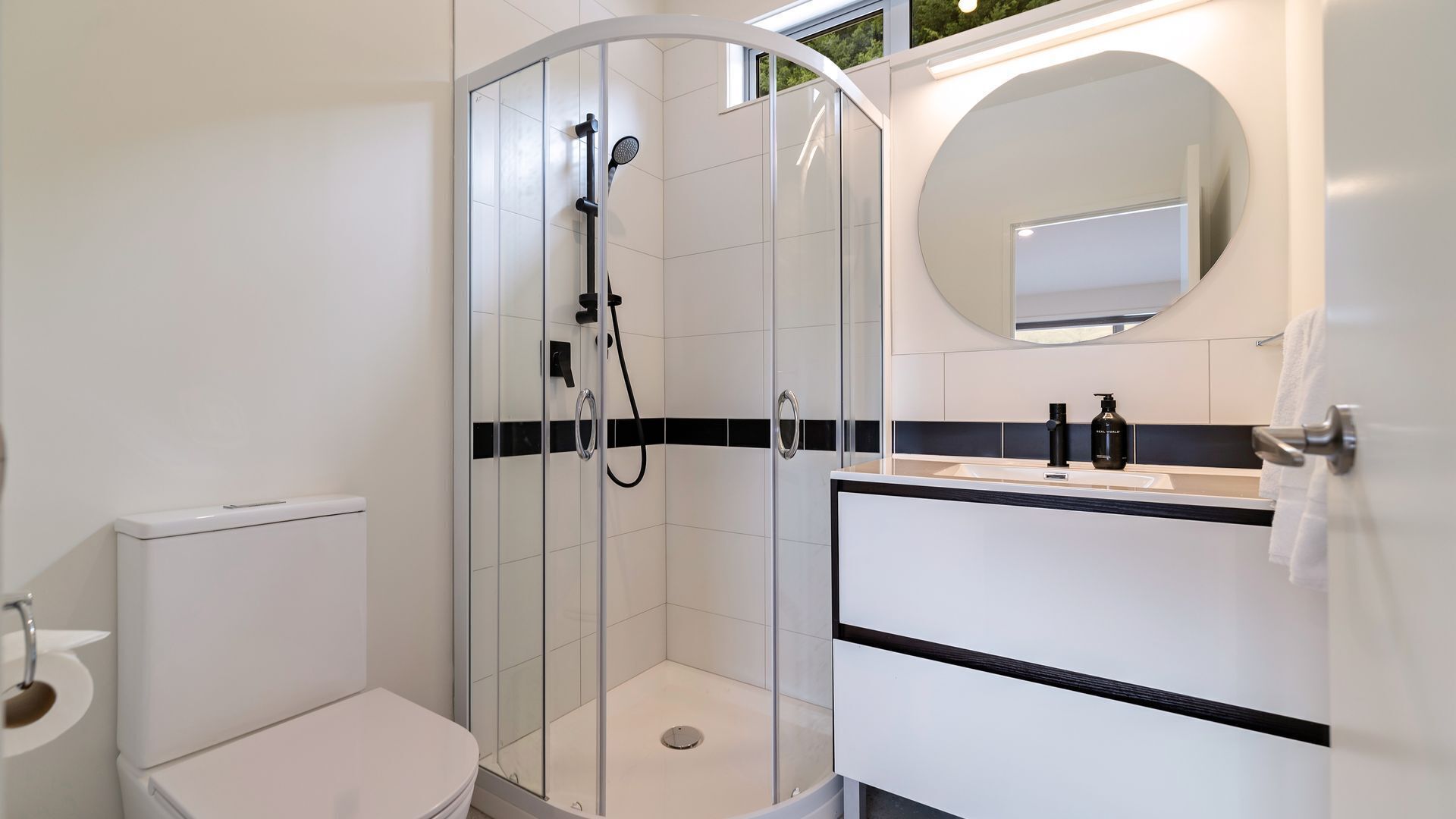 A modern bathroom with a glass-enclosed shower, a toilet, a sink with a mirror, and a towel rack.