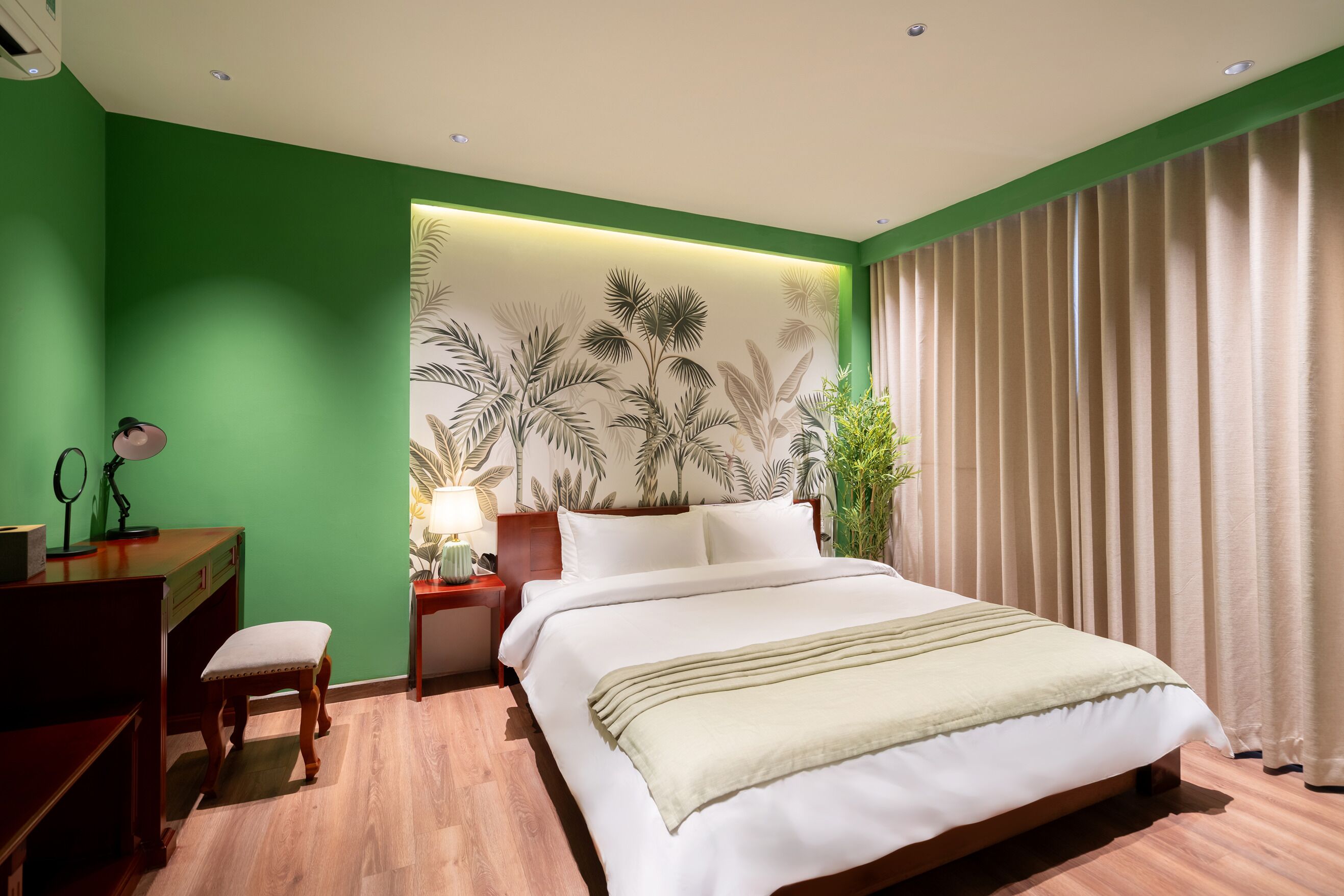 A hotel room with a bed, a desk, a chair, a nightstand, and a wall with a palm leaf pattern.