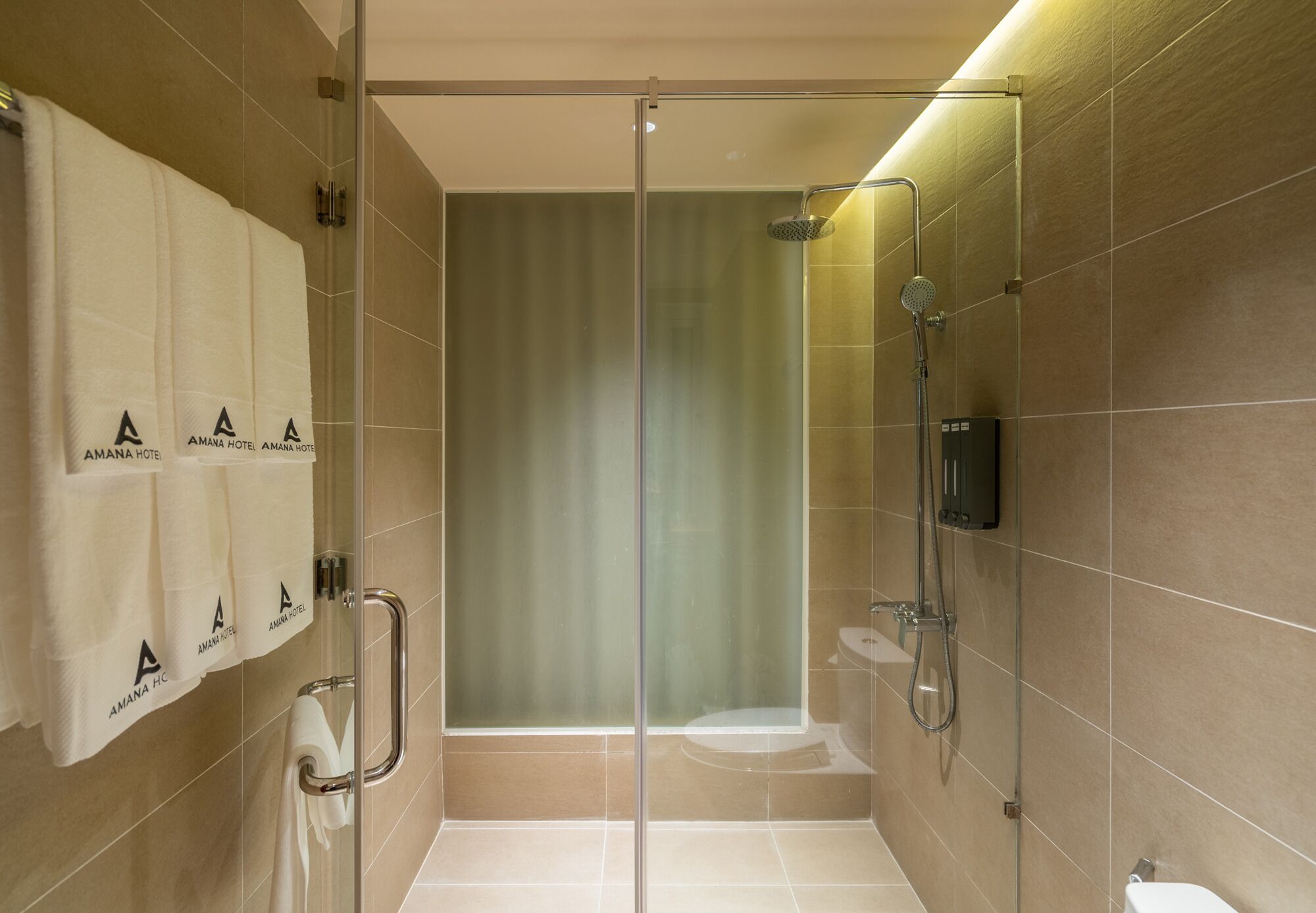 Een moderne badkamer met een douchecabine van glas, een toilet en een handdoekrek met handdoeken met een logo.