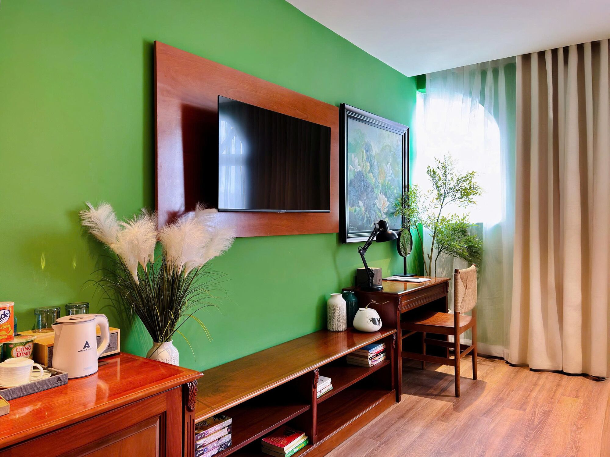 A room with a green wall, a wooden desk with books, a coffee maker, and a TV mounted above it.