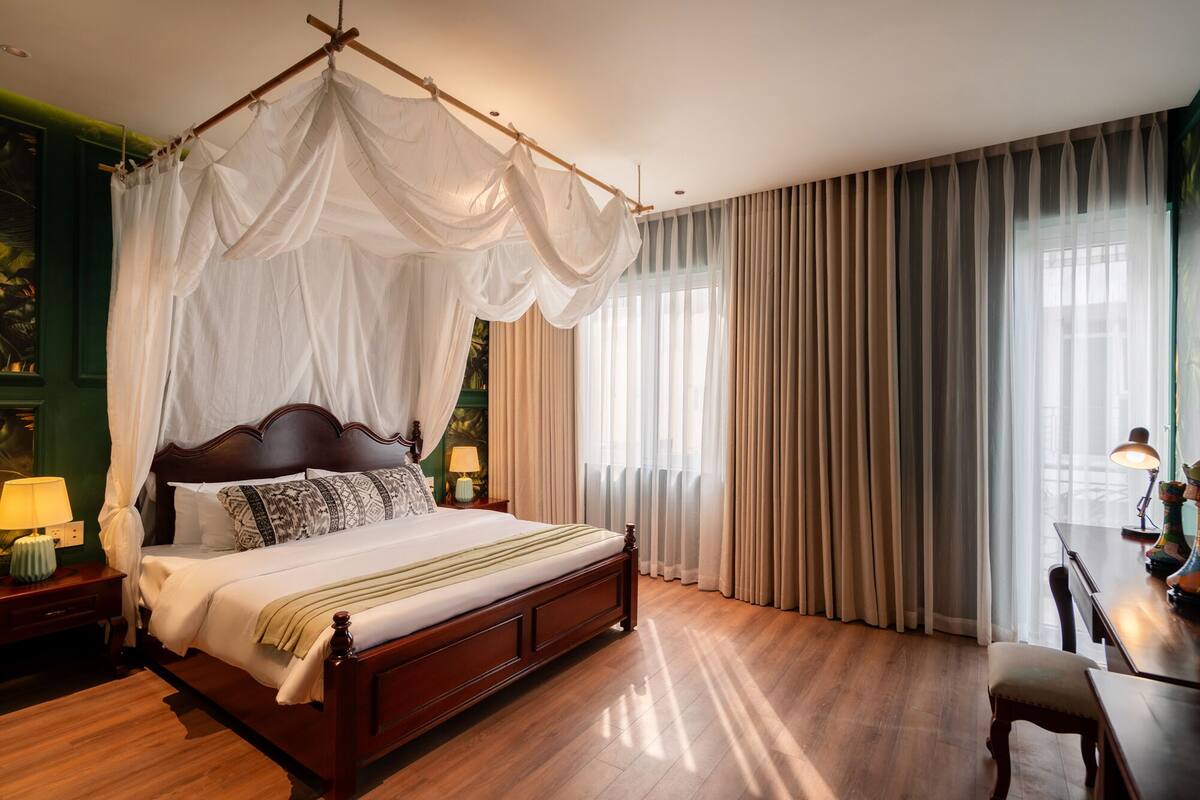 Une chambre spacieuse avec un grand lit, un plancher en bois, un lit à baldaquin et une vue sur l’extérieur grâce à de grandes fenêtres.