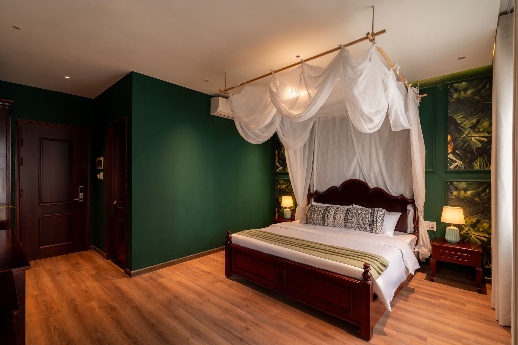 A bedroom with a four-poster bed, green walls, wooden flooring, and a nightstand with a lamp.