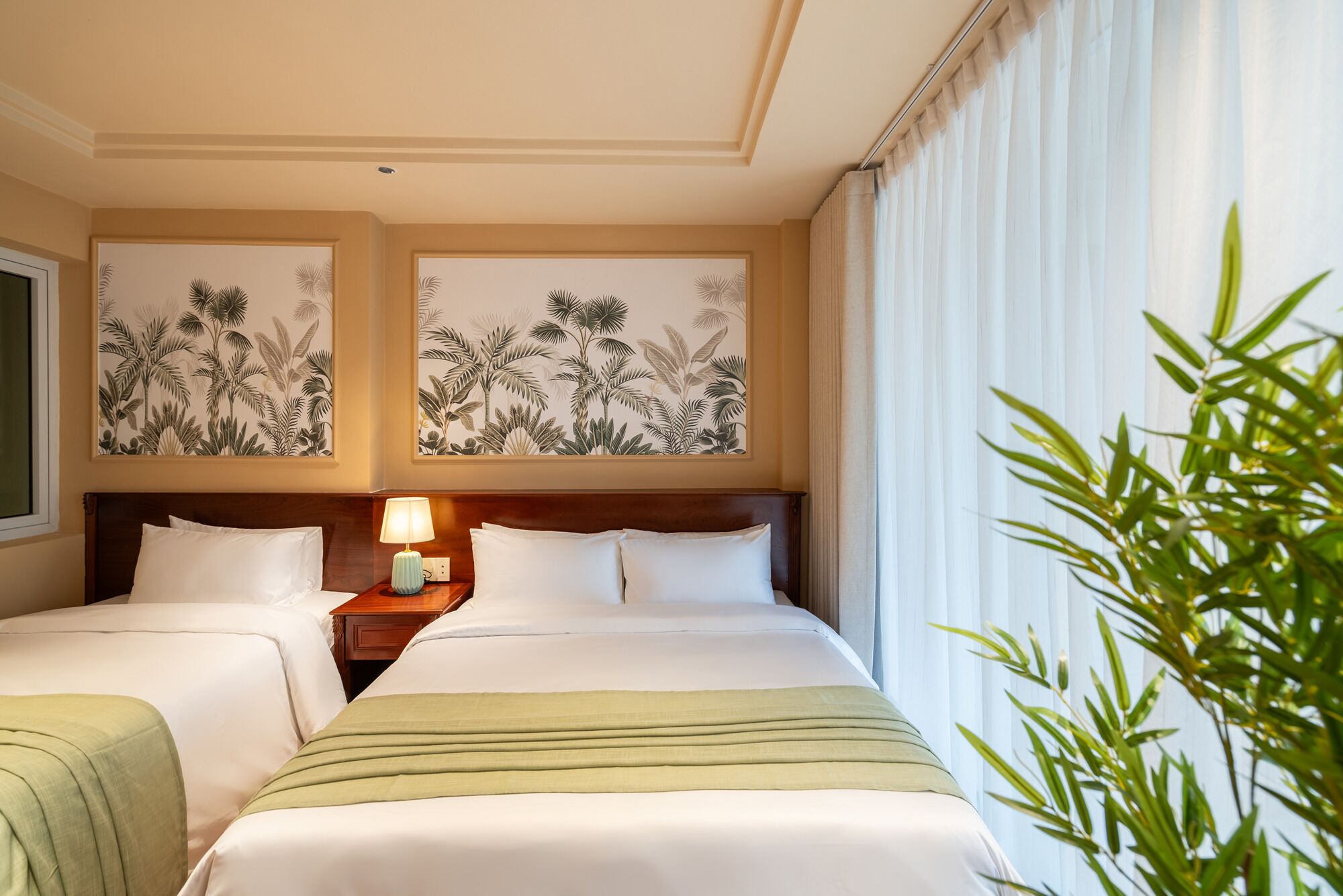 A hotel room with two beds, a nightstand, a lamp, and tropical-themed wall art.