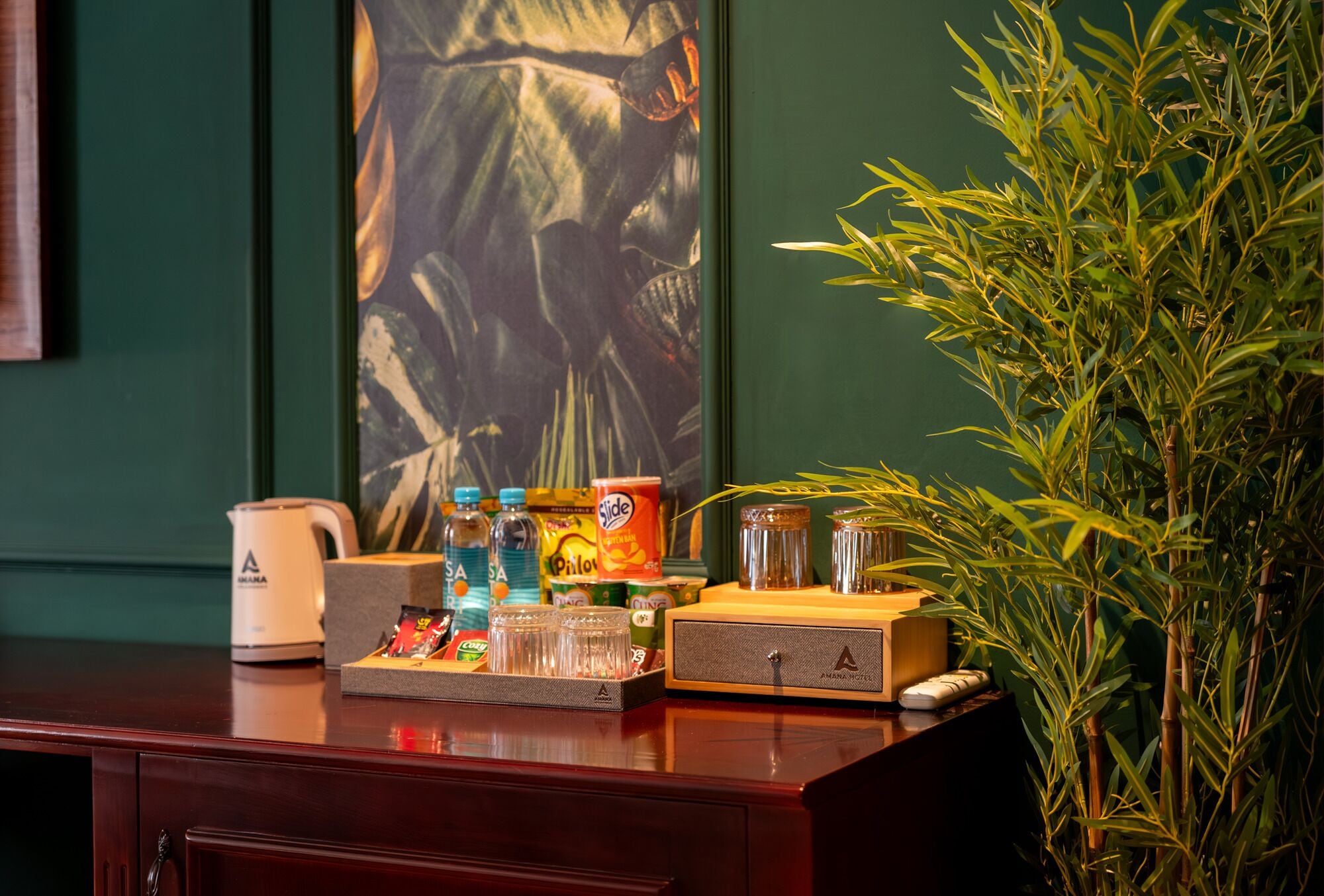 Un comptoir d’accueil d’hôtel avec une machine à café, un plateau de collations, une plante et un tableau accroché au mur.