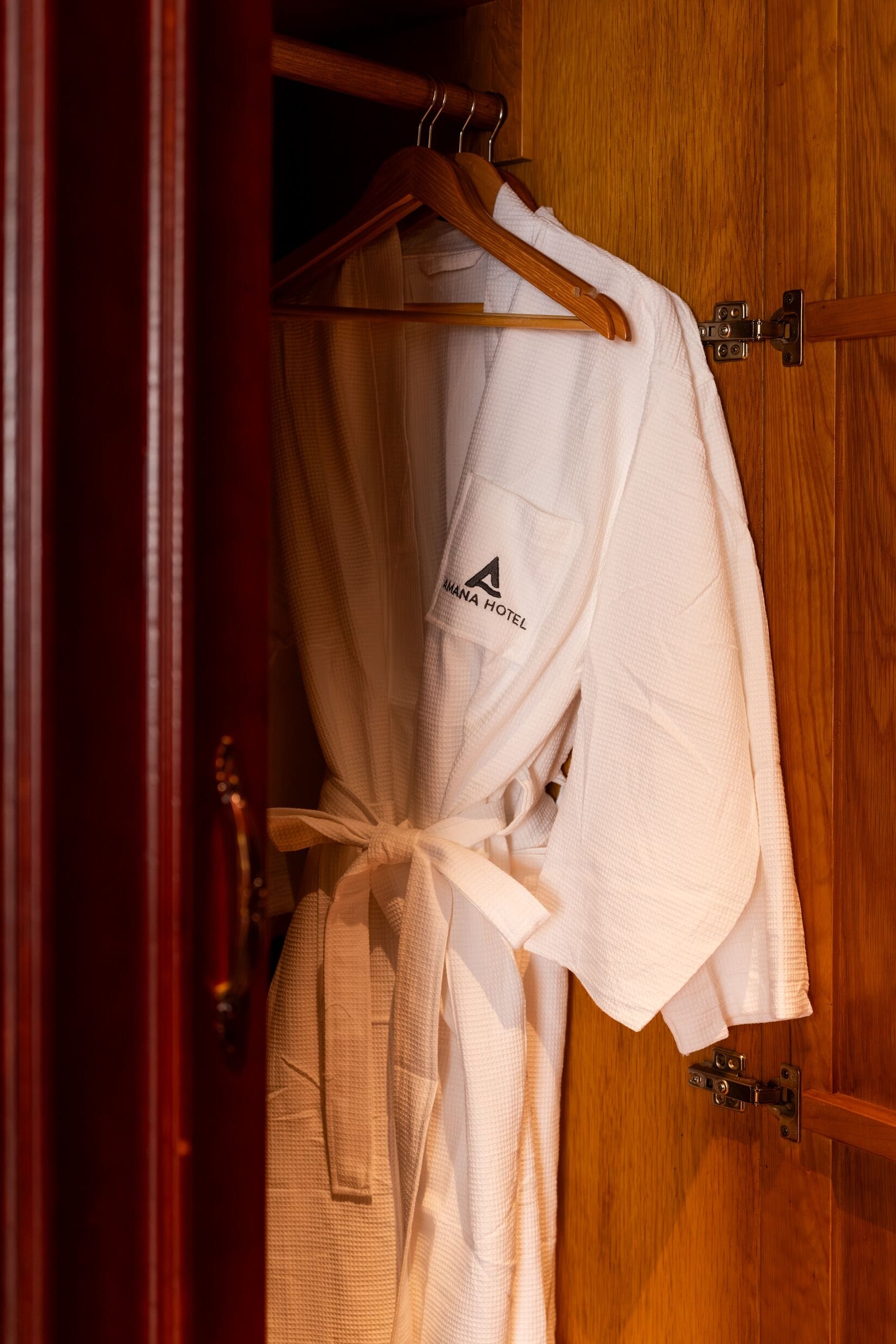 A wooden wardrobe with a white robe hanging on a wooden hanger.
